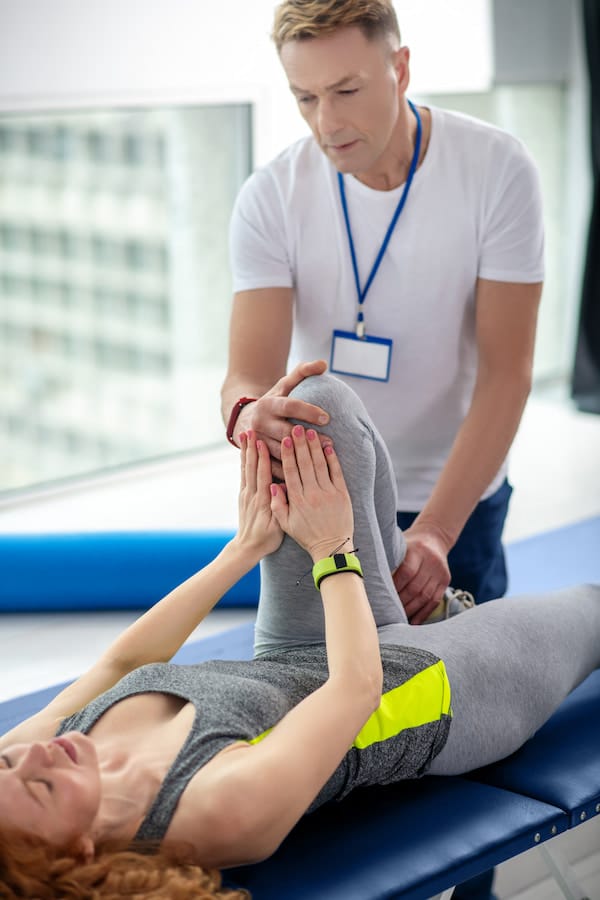 Physiotherapist Treating the knee of his female patient due to sport injury