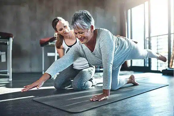 Physical therapist assisting an older adult with a balance and stability exercise during a therapy session.