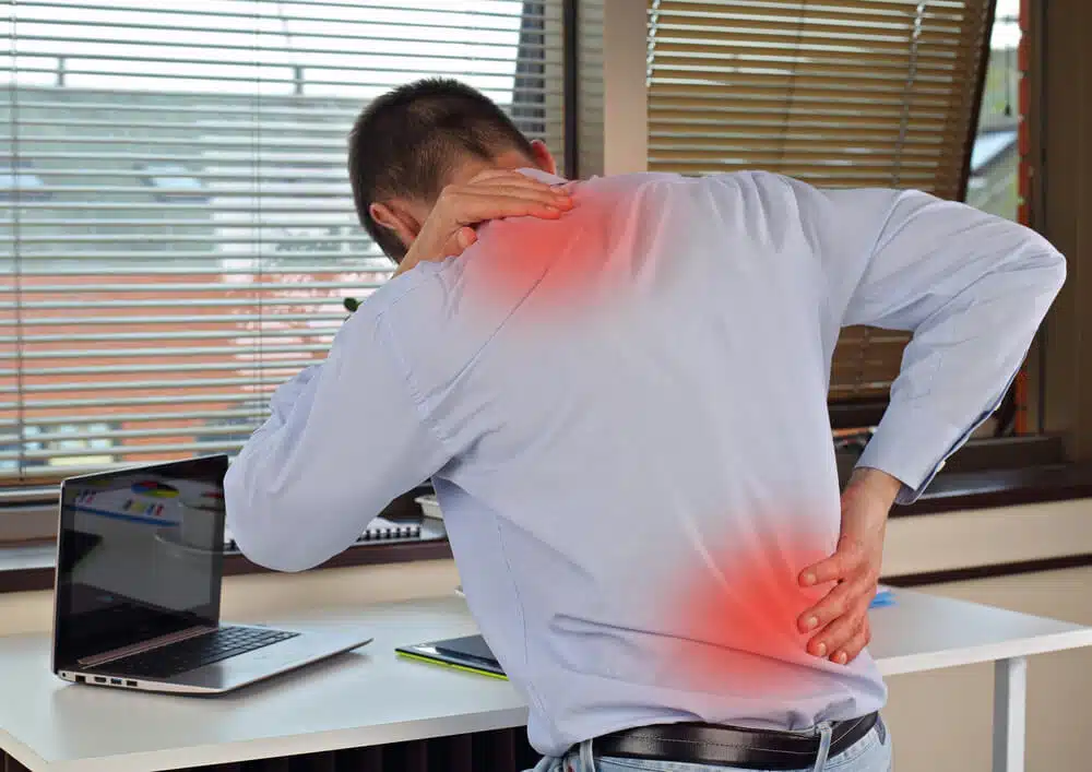 Office worker experiencing recurring neck and lower back pain from prolonged sitting and muscle strain.